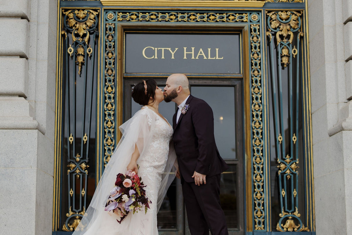 A bride and a groom kiss in front of San Francisco's majestic city hall.