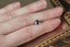 A natural cushion cut steely gray spinel available to add as a center stone for your heirloom setting at The North Way Studio. A steely blueish gray reminiscent of a stormy day. The spinel is shown resting on a woman's fingers for size reference.