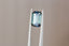 A natural emerald cut teal green sapphire available to add as a center stone for your heirloom ring setting at The North Way Studio. This stone has north and south poles of medium blue with the middle portion leaning more teal blue in its facets. The sapphire is shown tilted to the side and held with tweezers.