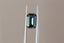 A natural emerald cut teal green sapphire available to add as a center stone for your heirloom ring setting at The North Way Studio. This stone has north and south poles of medium blue with the middle portion leaning more teal blue in its facets. The dark colored sapphire is shown facing the viewer and held with tweezers.