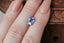 A glowing, faintly opalescent shade of light to medium blue emerald cut sapphire. This Sri Lankan sapphire is available for purchase alongside an heirloom setting at The North Way Studio. The sapphire is shown resting on a woman's fingers for size reference.