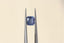 A natural periwinkle blue sapphire available to add as a center stone for your heirloom ring setting at The North Way Studio. A lovely periwinkle medium purple blue. The sapphire is shown held with tweezers and tilted to the side.