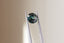 A natural round green teal sapphire available to add as a center stone for your heirloom setting at The North Way Studio. Shifting hues of teals, blues, and greens. The sapphire is shown held up by tweezers.