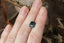 A natural emerald cut teal sapphire available to add as a center stone for your heirloom setting at The North Way Studio. A deeper forest teal hue. The sapphire is shown resting on a woman's fingers for size reference.