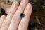 A natural emerald cut teal sapphire available to add as a center stone for your heirloom setting at The North Way Studio. A deeper forest teal hue. The sapphire is shown resting on a woman's fingers for size reference.