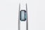 A natural elongated emerald cut teal Montana sapphire available to add as a center stone for your heirloom setting at The North Way Studio. Wisps of yellow and blue dance within this deep teal sapphire. The stone is shown held up by tweezers on a white background.