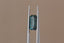 A natural elongated emerald cut teal Montana sapphire available to add as a center stone for your heirloom setting at The North Way Studio. Wisps of yellow and blue dance within this deep teal sapphire. The stone is shown held up by tweezers.