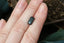 A natural elongated emerald cut teal Montana sapphire available to add as a center stone for your heirloom setting at The North Way Studio. Wisps of yellow and blue dance within this deep teal sapphire. The stone is shown resting on a woman's hand for size reference.