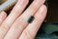 A natural elongated emerald cut teal Montana sapphire available to add as a center stone for your heirloom setting at The North Way Studio. Wisps of yellow and blue dance within this deep teal sapphire. The stone is shown resting on a woman's hand for size reference.