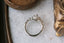Fantasy elven alternative engagement ring designed by The North Way Studio. This custom three stone engagement ring is shown in reclaimed white gold with an oval diamond center. This fairytale inspired design features hand-carved gold leaves, two natural pear cut diamonds, and a cluster of diamond dewdrops. Shown viewed from above.