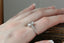 Fantasy elven alternative engagement ring designed by The North Way Studio. This custom three stone engagement ring is shown in reclaimed white gold with an oval diamond center. This fairytale inspired design features hand-carved gold leaves, two natural pear cut diamonds, and a cluster of diamond dewdrops. Shown worn on a woman's hand.