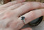A customizable fantasy solitaire engagement ring setting with small brilliant cut diamonds set into leaf prongs. Shown in reclaimed 14 karat yellow gold with an oval dark gray spinel worn on a woman's finger. Elven fairytale engagement ring designed by The North Way Studio.