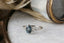This fantasy customizable engagement ring setting crafted by The North Way Studio features vines of reclaimed gold unfurling about genuine diamond dewdrops and a center stone chosen by the customer. This custom elven engagement ring is shown in 14 karat white gold with a gray spinel center.