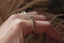 This antique inspired engagement ring setting crafted by The North Way studio features vines of reclaimed gold unfurling about genuine diamond dewdrops and a center stone chosen by the customer. This custom engagement ring is shown in 14 karat yellow gold with a gray spinel center worn on the index finger of a hand.