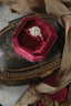This vintage inspired heirloom setting crafted by The North Way Studio features leaves carved in reclaimed gold, a halo of natural brilliant cut round diamonds, and two round natural diamond side stones strewn about a unique center stone. This custom antique style engagement ring is shown in 14 karat yellow gold with a round diamond center in a red ring box atop an antique jewelry box.