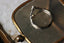 A dramatically tapered ring with leaves and a rustic carved band is topped with a pear cut diamond. Designed by The North Way Studio and shown here in white gold atop a mirror facing away from the viewer.