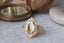 An 18k yellow gold ring, the Illuminated No. 1 by The North Way Studio, created in collaboration with Misfit Diamonds. This ring features a 2.01 carat natural portrait cut diamond surrounded by a halo of white diamonds and is detailed with hand-engraved floral carvings, archways, and an unfurling leaf band. The organic, relic-inspired design evokes a woodland glade.