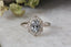 This heirloom engagement ring setting crafted by The North Way Studio features a shield halo of diamonds, engraved walls, and hand-carved leaves all strewn about a unique center stone of choice. This fantasy antique inspired engagement ring is shown in 14 karat white gold with a natural pale gray spinel center stone.