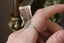 This heirloom engagement ring setting crafted by The North Way Studio features a shield halo of diamonds, engraved walls, and hand-carved leaves all strewn about a unique center stone of choice. This fantasy antique inspired engagement ring is shown in 14 karat white gold with a natural pale gray spinel center stone and worn on the index finger of a hand showing the side profile of the setting wall.