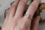 An antique inspired engraved engagement ring setting, customizable with choice of reclaimed fine gold and center jewel. Shown in 14 karat rose gold with lab grown oval diamond. Shown on the hand.