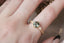 Teal green Montana sapphire and A natural Montana teal green sapphire and two natural marquise diamonds are set in 18 karat yellow gold in this nature inspired engagement ring. This ring features hand-carved gold leaves and bark texture. Ready to ship antique inspired alternative engagement ring, size 7. Shown on a woman's hand.