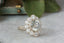 An antique inspired flower diamond halo engagement ring. This fairy garden engagement ring features a large natural gray diamond center with a diamond halo and hand-carved leaf and bark texture in 18 karat white gold. Ready to ship engagement ring crafted by The North Way Studio in collaboration with Claire Pettibone.