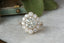 An antique inspired flower engagement ring featuring a large natural gray diamond center with a diamond halo and hand-carved leaf and bark texture in 18 karat white gold.