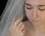 An antique inspired flower diamond halo engagement ring. This fairy garden engagement ring features a large natural gray diamond center with a diamond halo and hand-carved leaf and bark texture in 18 karat white gold. Ready to ship engagement ring crafted by The North Way Studio in collaboration with Claire Pettibone. Shown worn on the hand of a young woman in a veil.