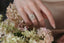 An antique inspired flower diamond halo engagement ring. This fairy garden engagement ring features a large natural gray diamond center with a diamond halo and hand-carved leaf and bark texture in 18 karat white gold. Ready to ship engagement ring crafted by The North Way Studio in collaboration with Claire Pettibone. Shown on a woman's hand.