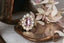 A flower engagement ring in natural pink spinel with diamond halo and sapphire leaves, hand carved leaves and bark texture in 18 karat yellow gold.
