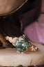 This custom heirloom engagement ring setting designed and crafted by The North Way Studio features delicate leaves carved in reclaimed gold and a cluster of diamond dew drops spun about your choice of center gemstone. This fantasy ring is shown cast in 14 karat rose gold and resting at a tilt with sunlight reflecting in the oval green sapphire center stone.