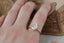 This custom heirloom engagement ring setting designed and crafted by The North Way Studio features delicate leaves carved in reclaimed gold and a cluster of diamond dew drops spun about your choice of center gemstone. This fantasy ring is shown in 14 karat yellow gold with a large pear cut diamond center and worn on the index finger of a hand resting on an antique gold jewelry box.