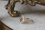 This custom fantasy engagement ring setting crafted by The North Way Studio features unfurling rustic leaves of hand-carved gold, rustling below a halo of natural white rose cut diamonds strewn about a uniquely chosen center stone. This variation of the Scrying Mirror ring is cast in 14 karat yellow gold and strewn about a teal rose cut sapphire. The engagement ring is shown facing the viewer's left and resting on a marble table.
