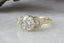 This custom heirloom engagement ring setting designed and crafted by The North Way Studio features two crescent diamonds and unfurling leaves of gold spun about a uniquely chosen center gemstone. This celestial fantasy ring is shown cast in 18 karat green gold with a brilliant cut round diamond center. The ring is viewed close up as it rests facing slightly left.