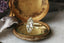 This heirloom engagement ring setting crafted by The North Way Studio features unfurling leaves and bark of carved gold, with petite claws to embrace a uniquely chosen center stone. This mythical ring is shown in 18 karat yellow gold with a large antique marquise old mine cut diamond center. The fantasy style engagement ring is resting on an antique mirror on a marble table.