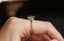 This nature inspired custom heirloom engagement ring setting crafted by The North Way Studio features unfurling leaves and bark of carved gold, with petite claws to embrace a uniquely chosen center stone. This mythical ring is shown in 14 karat yellow gold with an oval opalescent teal sapphire center. The fantasy engagement ring is shown worn on a woman's first finger.