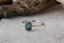 This custom heirloom engagement ring setting crafted by The North Way Studio features unfurling leaves and bark of carved gold, with petite claws to embrace a uniquely chosen center stone. This mythical ring is shown in 14 karat white gold with a teal blue sapphire center. The fae inspired engagement ring is shown resting on a marble table facing slightly left.