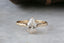 This heirloom engagement ring setting crafted by The North Way Studio features unfurling leaves and bark of carved gold, with petite claws to embrace a uniquely chosen center stone. This mythical ring is shown in 14 karat yellow gold with a pear cut diamond center. The alternative engagement ring is shown close up resting on a marble table providing a view of the claw prongs.
