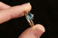 This nature inspired custom heirloom engagement ring setting crafted by The North Way Studio features unfurling leaves and bark of carved gold, with petite claws to embrace a uniquely chosen center stone. This mythical ring is shown in 14 karat yellow gold with an oval opalescent teal sapphire center. The fantasy engagement ring is shown held between an index finger and thumb on a black background.