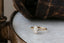 This custom heirloom engagement ring setting crafted by The North Way Studio features unfurling leaves and bark of carved gold, with petite claws to embrace a uniquely chosen center stone. This magical ring is shown in 14 karat yellow gold with a pear cut diamond center. The fantasy engagement ring is shown resting on a marble table with an antique worn leather case in the background.