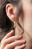 A small gold charm with natural green tourmaline and hand-carved leaf details. Shown hanging on The Fae Hoop earrings on a woman's ear.