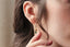 A small gold charm with natural green tourmaline and hand-carved leaf details. Shown in yellow gold hanging on The Fae Hoop earring on a woman's ear.