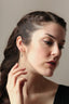 A small gold charm with lab grown pear diamond and hand-carved leaf details. Shown in white gold hanging on the Fae Hoop earrings on a woman's ear.