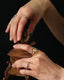 A hand wearing elegant gold rings is opening a jar delicately. 
