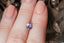 A faintly silky purple and pink natural pear cut sapphire available at The North Way Studio to be added to your custom heirloom setting. Shown resting on a woman's fingers for reference.
