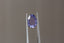 A uniquely shaped, lush portrait-cut sapphire in a regal purple hue. This sapphire is available for purchase alongside an heirloom setting at The North Way Studio. The sapphire is shown held up by tweezers.