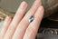 A natural steely blue marquise sapphire available to add as a center stone for your heirloom setting at The North Way Studio. A medium steely blue with whispers of teal. The sapphire is shown resting on a woman's fingers for size reference.