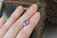 A natural oval light purple and pink sapphire available to add as a center stone for your heirloom ring setting at The North Way Studio. A lovely pale lilac pink with perhaps a hint of opalescence at some angles. The sapphire is shown resting on a woman's hand for size reference.