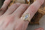 A solitaire engagement ring setting with hand-carved leaves and elongated shield shaped gold halo. 
Shown with a natural marquise opalescent blue sapphire. 