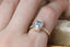 A blue sapphire ring designed and crafted by The North Way Studio in collaboration with Claire Pettibone and cast in reclaimed gold is shown upon a hand in a closeup of the ring.